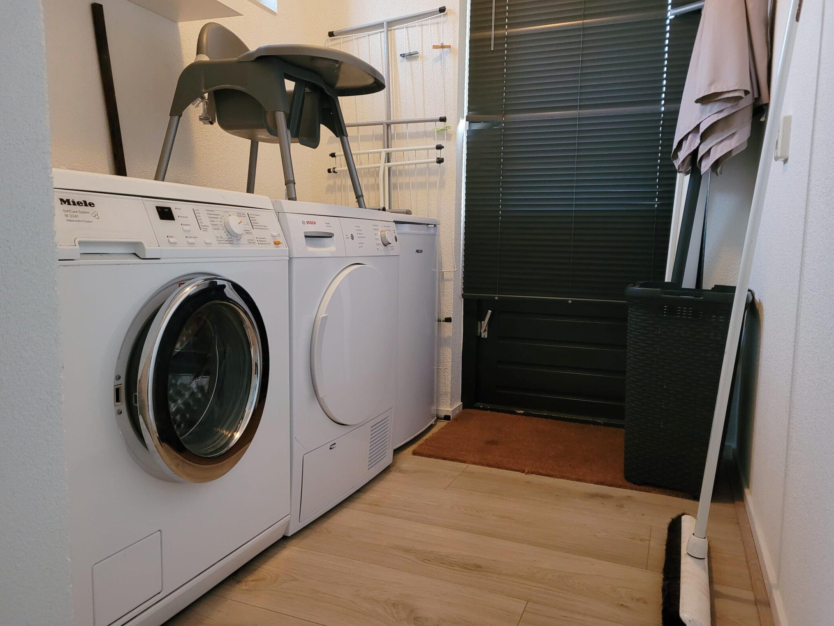 Une petite buanderie équipée d’un lave-linge à chargement frontal, d’un sèche-linge et d’un petit espace dédié au repassage.