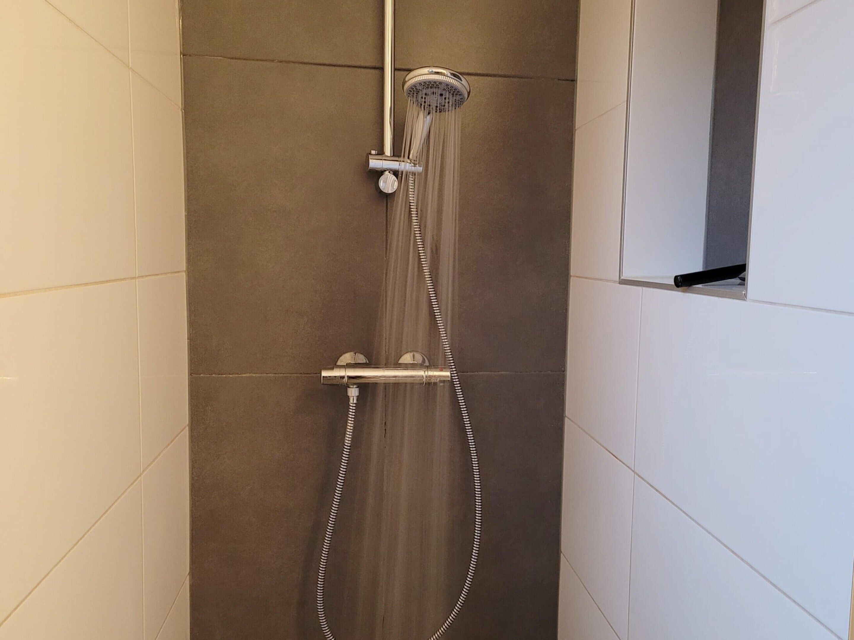 A shower with a handheld showerhead and a wall-mounted control.