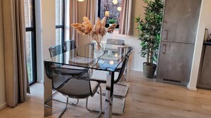 Une cuisine moderne avec une table à manger en verre, des chaises, un réfrigérateur et une plante en pot.