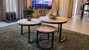 Un salon moderne avec un téléviseur, deux tables rondes, un saladier de fruits et une lampe.
