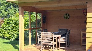Une terrasse en bois avec une table et des chaises, un jeu de fléchettes et une petite étagère.