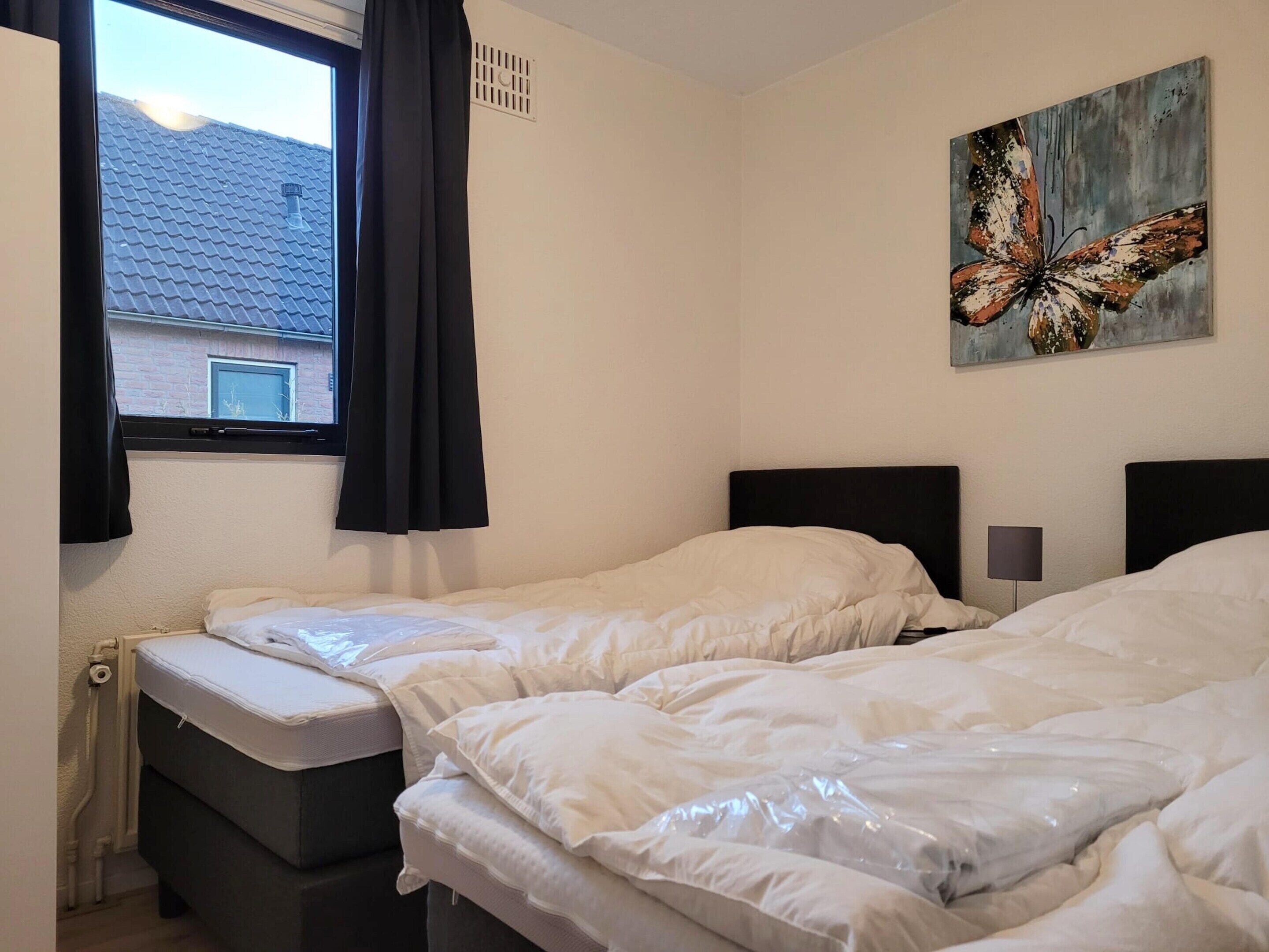 Una camera d'albergo con due letti, una finestra con tende, un quadro appeso al muro e un comodino con una lampada.