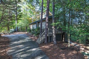 A cabin surrounded by tall trees, with a wooden deck and a staircase leading to the entrance. - Cozy TreeTop Cabin - (Helen)
