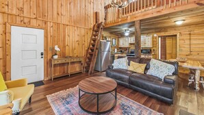Een houten chalet van binnen met een zithoek, keuken en een balkon.
