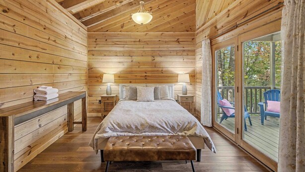 Een houten slaapkamer met een groot bed, een bankje, bedlampjes en uitzicht op de natuur.