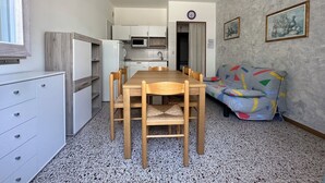 A compact living space with a kitchenette, a dining area with a wooden table and chairs, and a sofa with a colorful geometric pattern. - Bibione apartment close to promenade (Bibione)