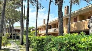 A pathway leading to a building with multiple balconies and a garden area with trees and shrubs. - Bibione flat with pool access (Bibione)