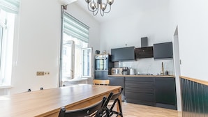 A modern kitchen with a wooden dining table and chairs, a built-in oven, microwave, and a large window with blinds. - 3BR Apt 15 Min from Landstraße Hub (Vienna)