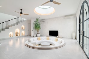 A modern living room with a circular seating area, a staircase, and a flat-screen TV. - Casa Contenta Canggu (Canggu)