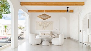 A modern interior with a white color scheme, featuring a seating area with white sofas and a round table, a hanging light fixture, and a large abstract painting on the wall. - Casa Contenta Canggu (Canggu)