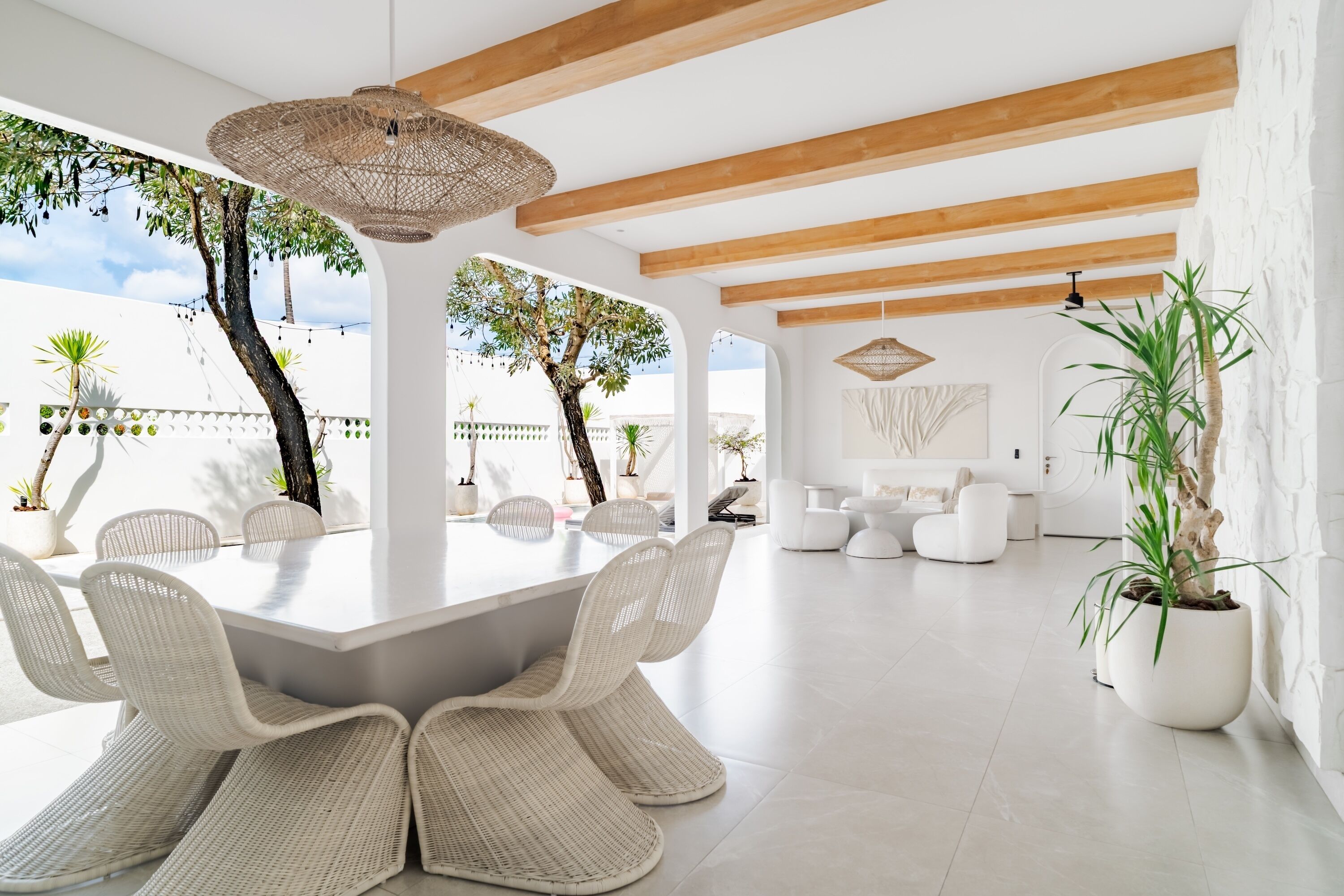 Un'ampia sala da pranzo con un tavolo bianco e sedie in vimini, un lampadario e vista sull'esterno.