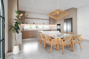 A modern kitchen with a central island, wicker chairs, and a hanging light fixture. - Casa Contenta Canggu (Canggu)