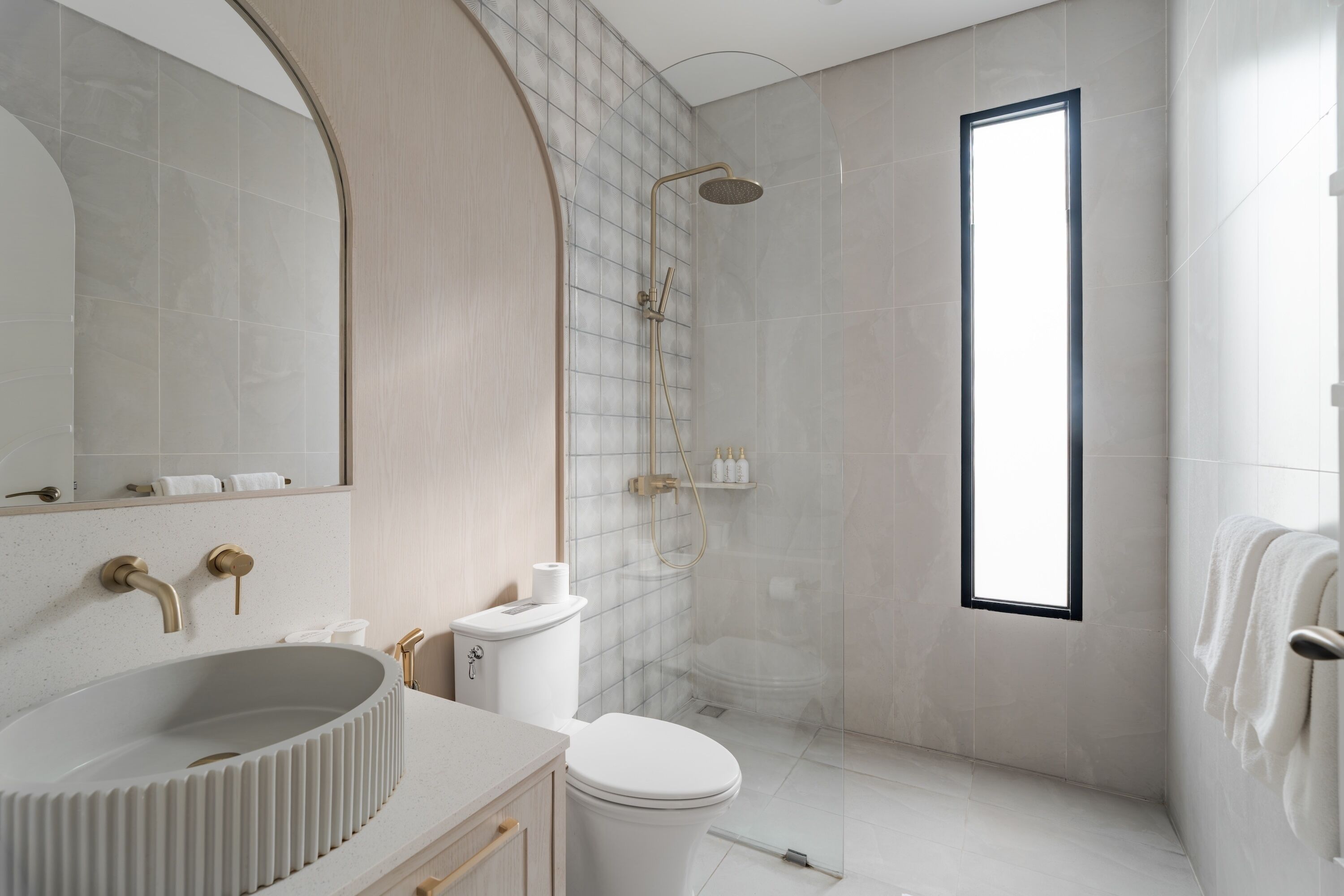 A modern bathroom with a freestanding toilet, a sink with a curved basin, a shower with a glass door, and a large window providing natural light.
