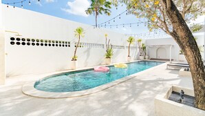 A swimming pool with a curved edge, surrounded by a white wall with decorative circular cutouts. There are potted plants and a tree with yellow flowers. - Casa Contenta Canggu (Canggu)