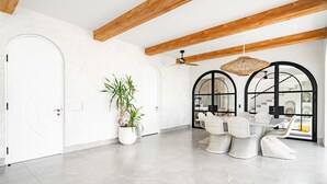 A spacious room with a modern design, featuring a white door, a potted plant, a dining area with wicker chairs, and a ceiling fan. - Casa Contenta Canggu (Canggu)