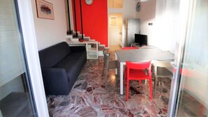 Ein modernes Wohnzimmer mit einer schwarzen Couch, einer roten Akzentwand, einer Treppe und einem Essbereich mit Tisch und Stühlen.