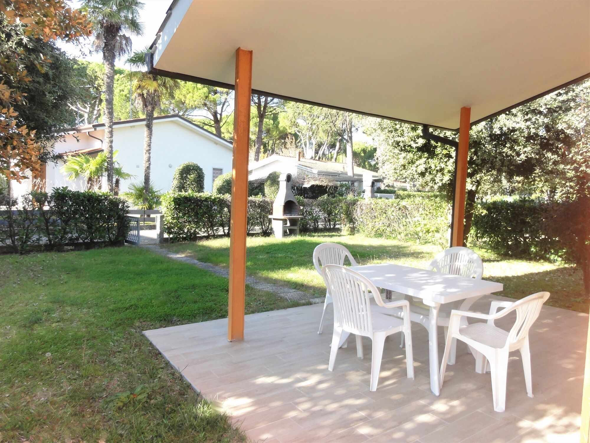 Un patio al aire libre con una mesa y sillas, rodeado de un jardín y una casa al fondo.