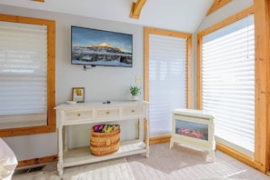 Une pièce avec un plafond en bois, une console blanche dotée de tiroirs, un panier en osier, un petit radiateur blanc et un tableau encadré accroché au mur.