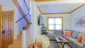 Una sala de estar con una escalera, un sofá, una mesa de centro y un televisor.