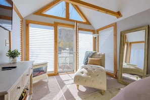 A room with a high ceiling, wooden beams, a large window, a plush armchair, a small table, and a mirror. - The Porch House, hot tub, pet friendly, historic! (Crested Butte)