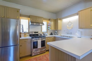 A kitchen with wooden cabinets, a stainless steel refrigerator, a stove, and a large island with a sink.