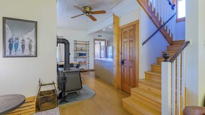 Amplia sala de estar con escalera de madera, ventilador de techo y una zona de cocina con parrilla.