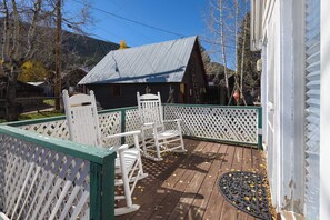 A wooden deck with rocking chairs and a metal doormat, surrounded by a white lattice fence. - The Porch House, hot tub, pet friendly, historic! (Crested Butte)