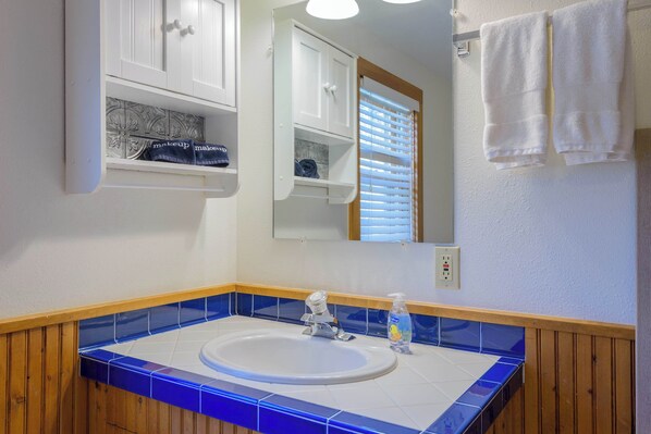 A bathroom with a white sink, blue-tiled countertop, wooden paneling, a mirror, and a towel rack. - The Porch House, hot tub, pet friendly, historic! (Crested Butte)