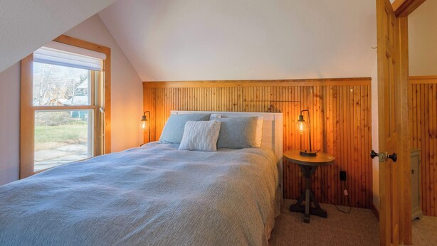 Un dormitorio con cama, dos lámparas de noche, una mesita y una ventana con vistas al exterior.