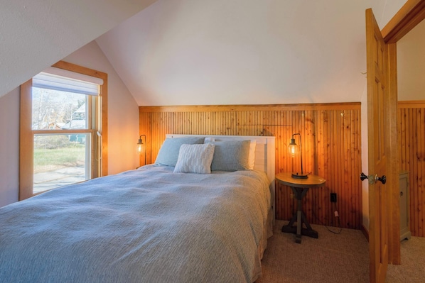 A bedroom with a bed, two bedside lamps, a small table, and a window with a view of the outdoors.