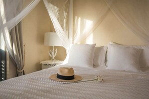 A bed with a white bedspread, a hat, and a white flower on the bed.