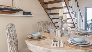 Un coin repas avec une table ronde, de l’assiette et des bols blancs, et une maquette de bateau accrochée au mur.