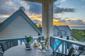 A balcony with a table set for two, a potted plant, and a bottle of champagne.
