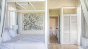 Une chambre à coucher avec un lit à baldaquin, un grand tableau représentant des motifs floraux, un dressing et un couloir menant à une autre pièce.