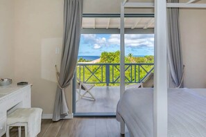 A bedroom with a bed, a desk, and a view of the ocean.