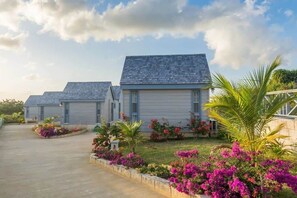 A row of single-story buildings with a flat roof, surrounded by well-maintained gardens with flowering plants.