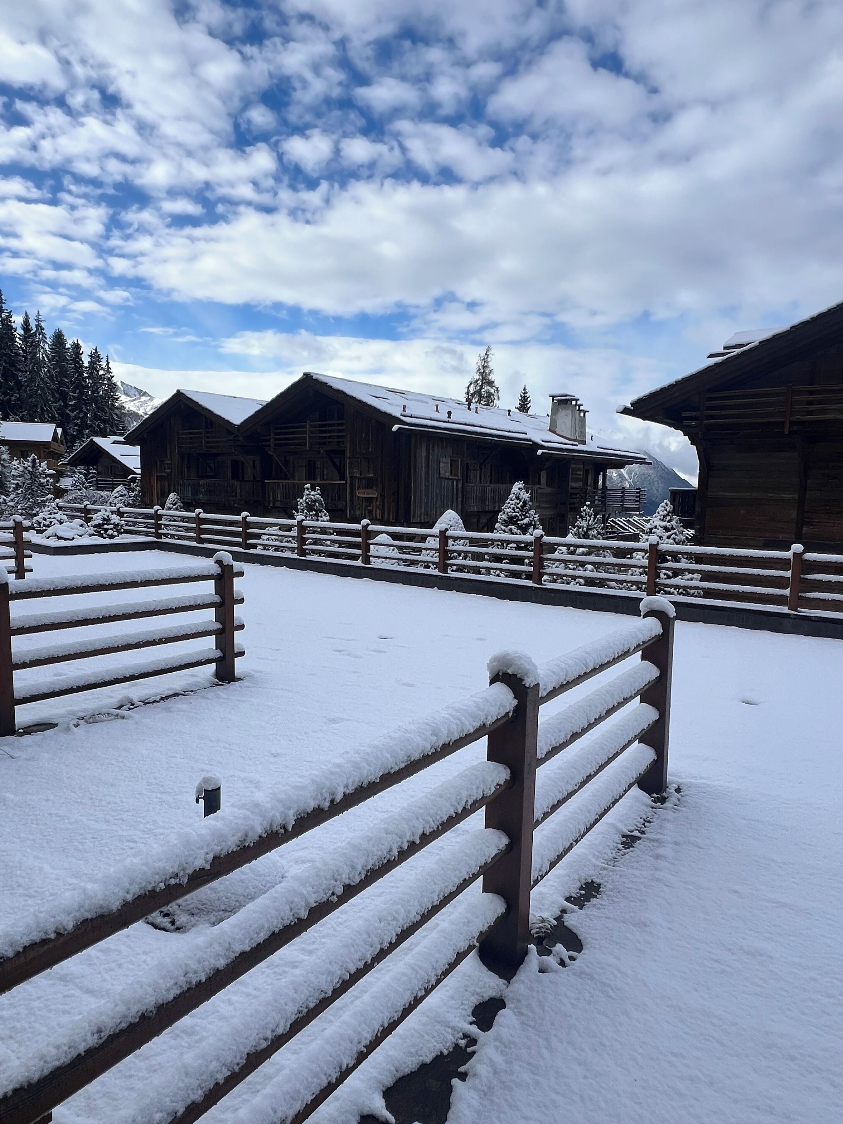 Un espace composé de cabanes en bois recouvertes de neige, avec des bancs et une clôture en bois.