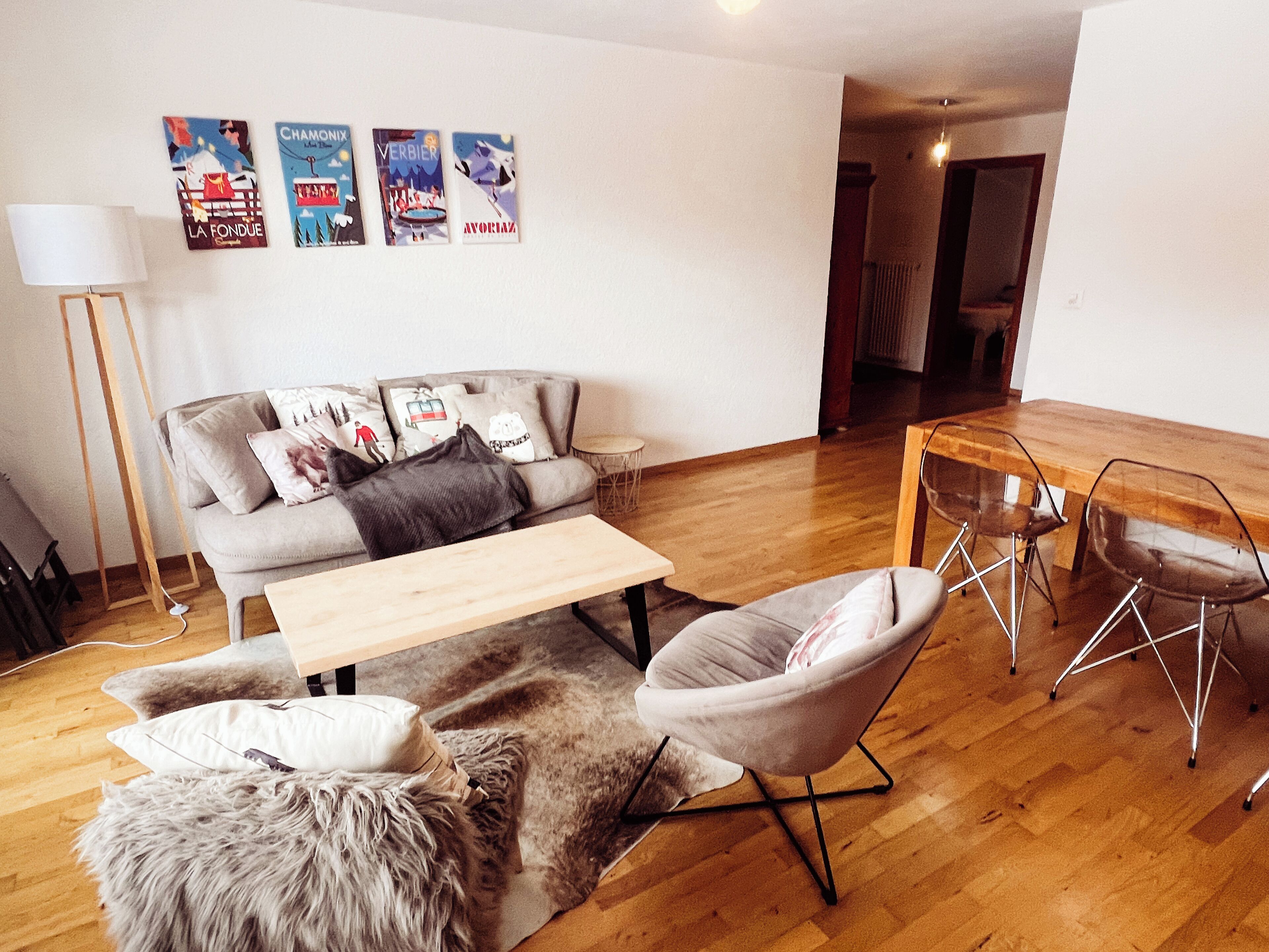 Un salon moderne comprenant un canapé, une table basse, un pouf moelleux et un coin repas avec une table et des chaises en bois.