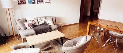 Un salon moderne comprenant un canapé, une table basse, un pouf moelleux et un coin repas avec une table et des chaises en bois.