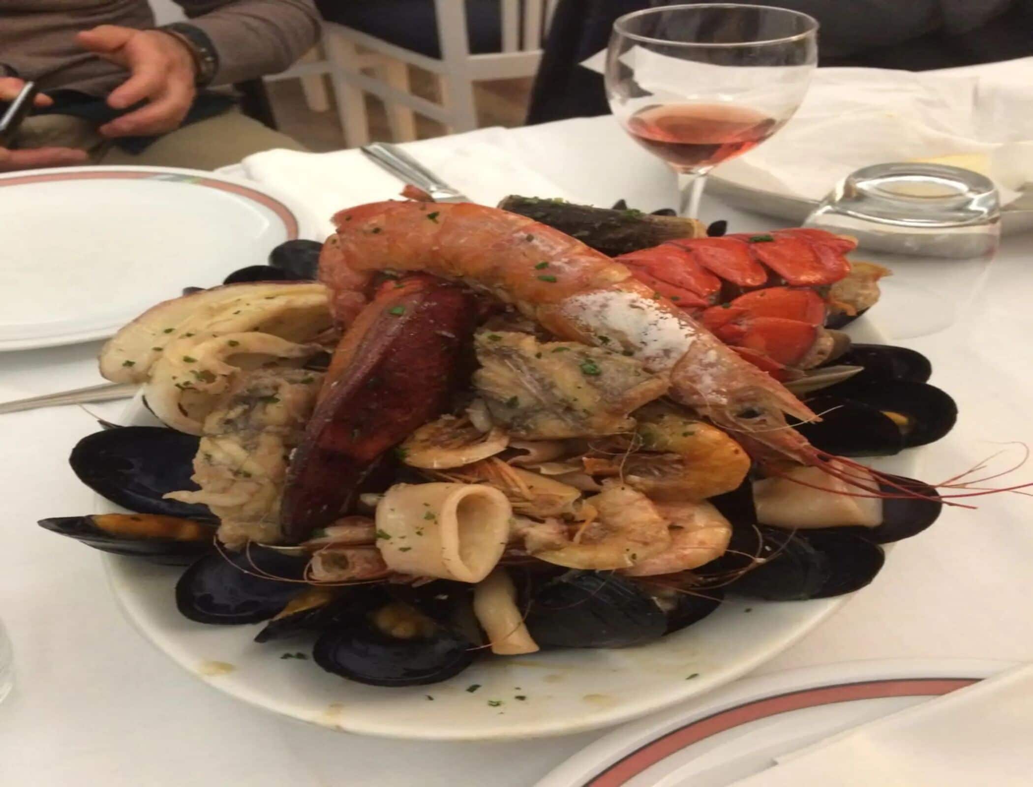 Una bandeja de mariscos con diversos moluscos y una copa de vino sobre una mesa.