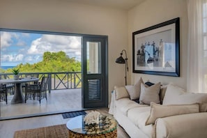 A living room with a sofa, a coffee table, a framed picture, and a view through a glass door to an outdoor area with a table and chairs.