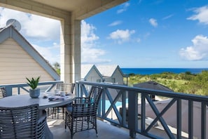 A balcony with a table and chairs, a potted plant, and a view of the ocean and beach.