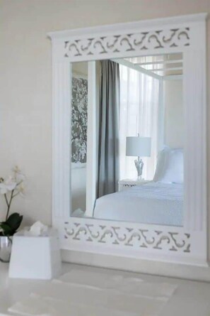 Ein Hotelzimmer mit einem großen Spiegel, einem Nachttisch mit Lampe, einem Bett mit weißer Bettwäsche und einer Vase mit Blumen.