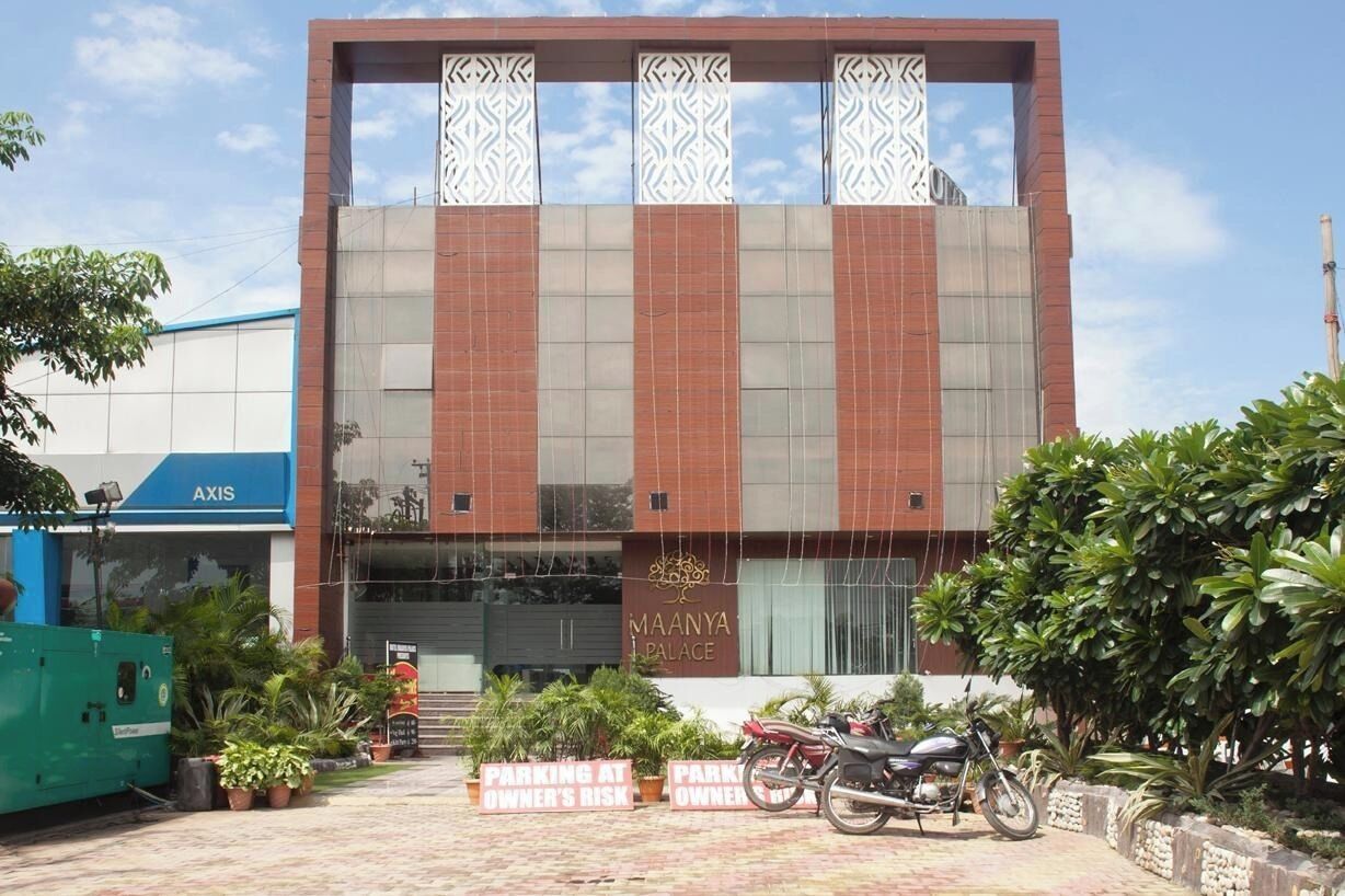Un edificio moderno con un letrero que dice "MAANYA PALACE" y un cartel de estacionamiento que indica "ESTACIONAMIENTO BAJO LA RESPONSABILIDAD DEL PROPIETARIO".