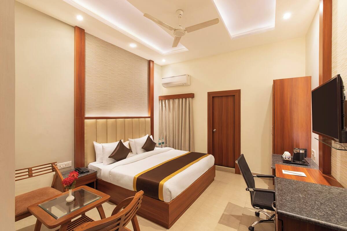 A hotel room with a bed, a desk with a chair, a television, and an air conditioning unit.