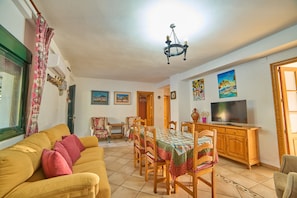 Un salon comprenant un canapé, une table à manger, des chaises, un téléviseur et des œuvres d’art accrochées aux murs.