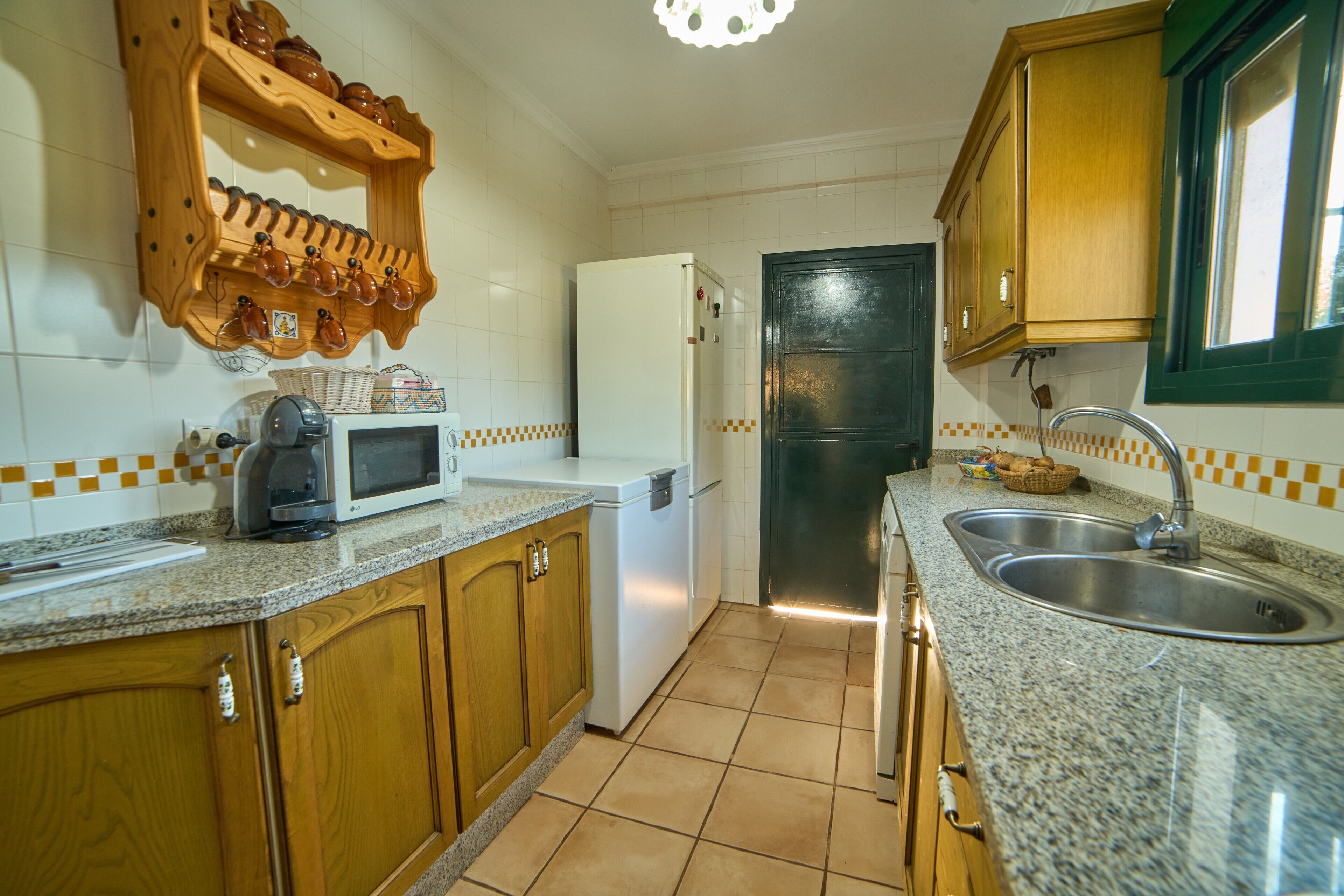 A kitchen with wooden cabinets, a microwave, a refrigerator, a sink, and a tiled backsplash.