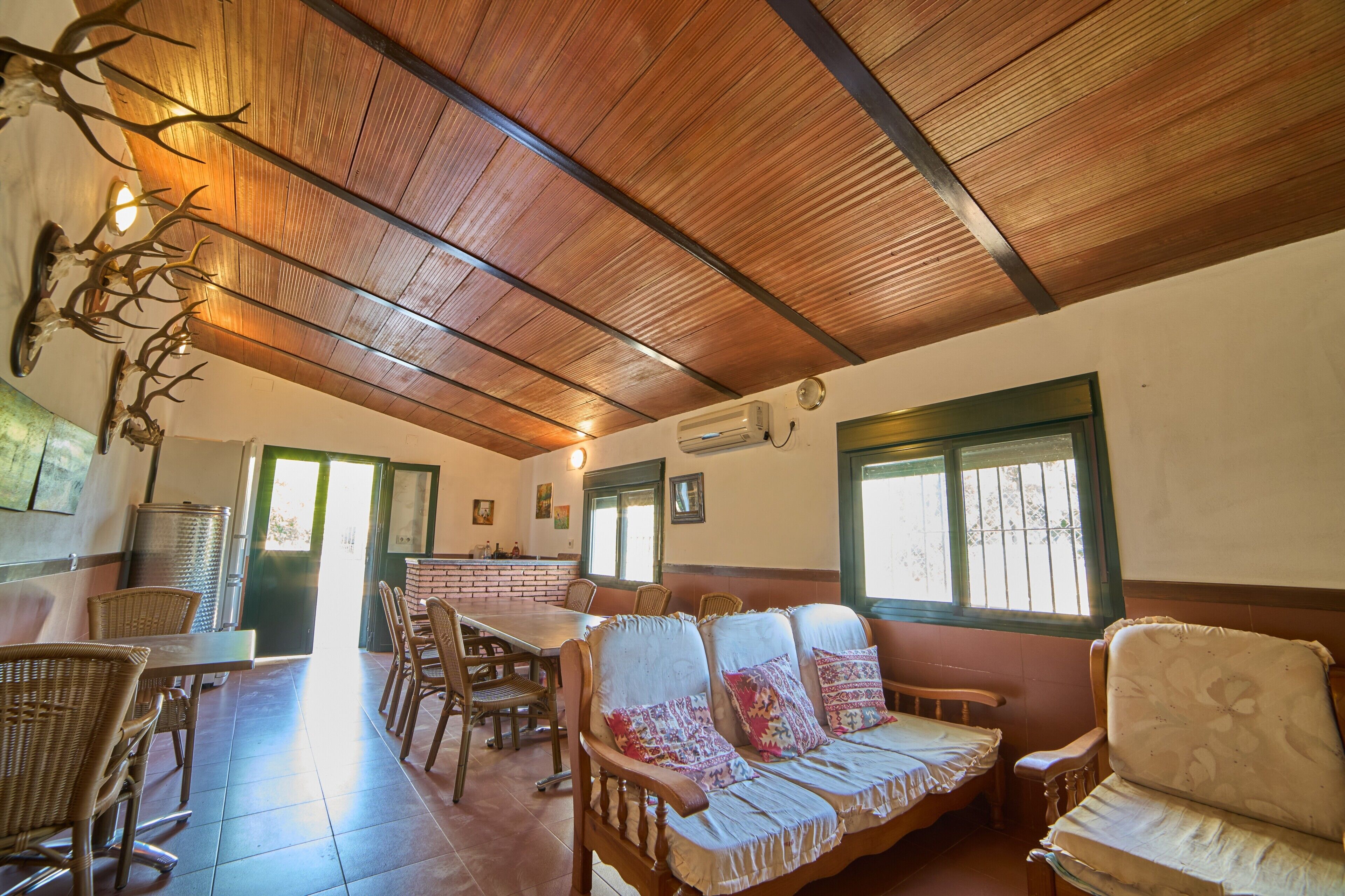 Un comedor con techo de madera, muebles de mimbre y pared de ladrillo.