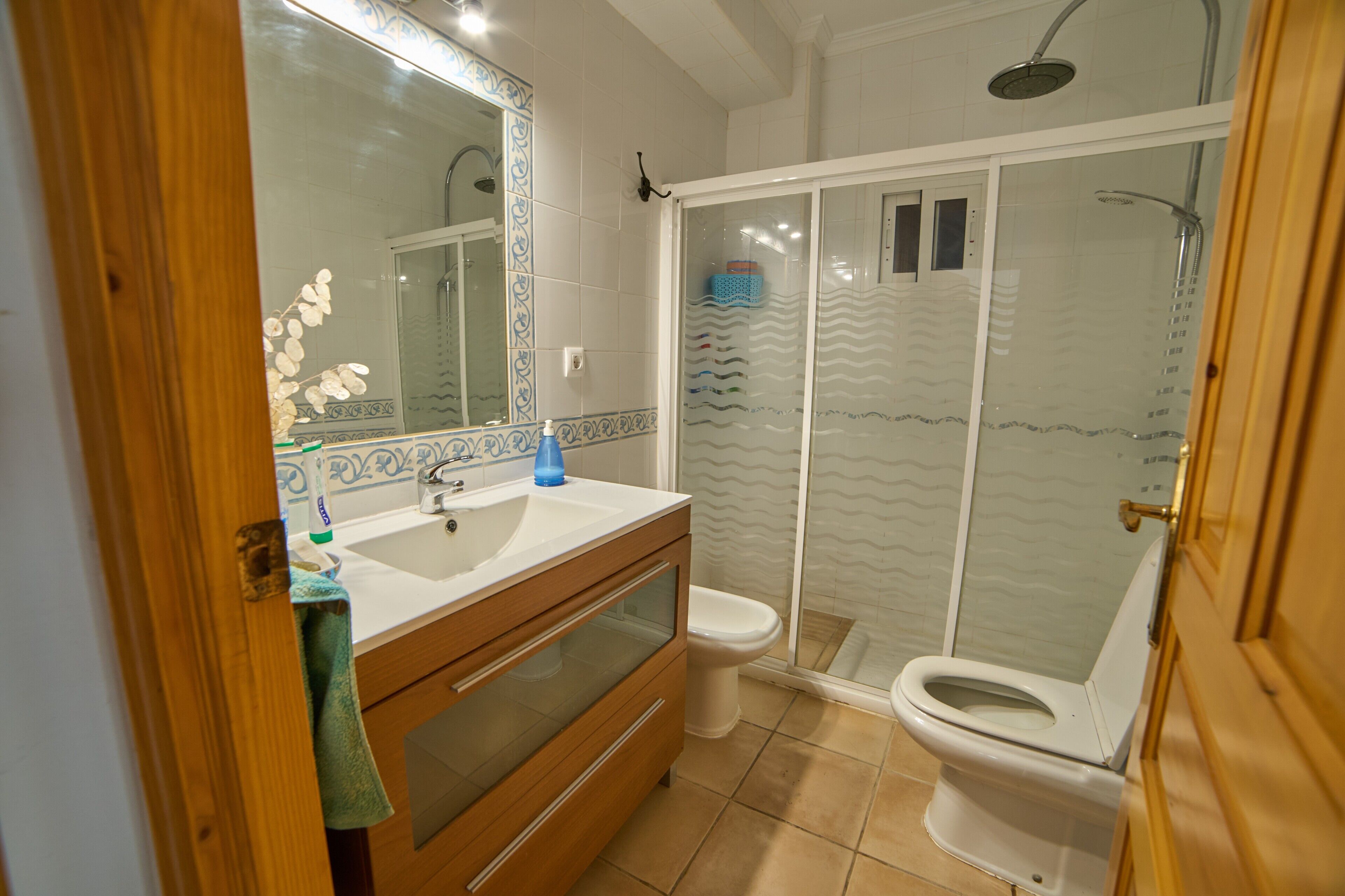 A bathroom with a shower, toilet, sink, and mirror.