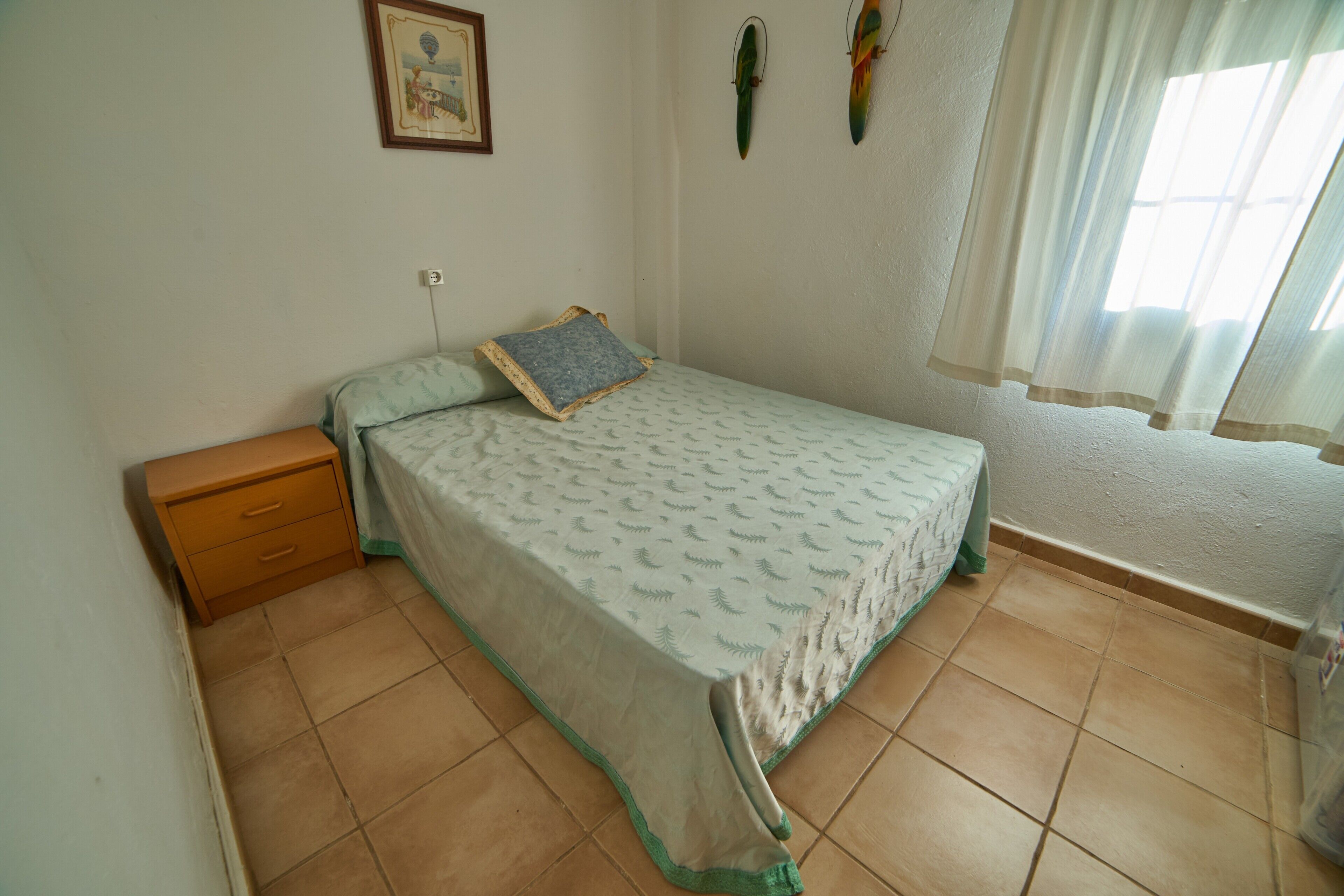 Una camera da letto con un letto, un comodino, un quadro appeso al muro e una finestra con tende.